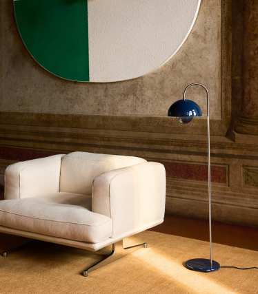 Elegante &Tradition vloerlamp naast moderne loungestoel in warm interieur.