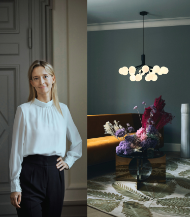 Portret van ontwerpster Sofie Refer naast een lichtgevende hanglamp van Nuura in een stijlvol interieur met bloemenaccenten.