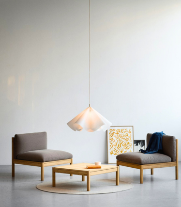 Hanglamp boven lage fauteuils in een rustige, minimalistische kamer.