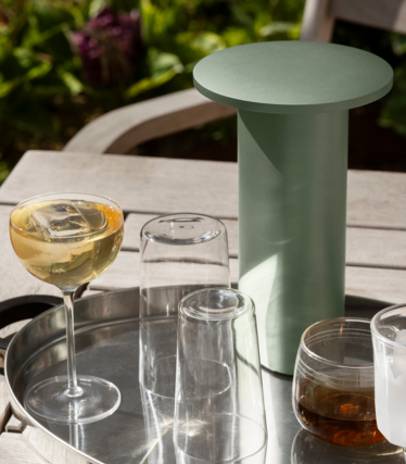 Saliegroene cilindervormige bijzettafel/koeler op een dienblad met glazen en drankjes buiten.